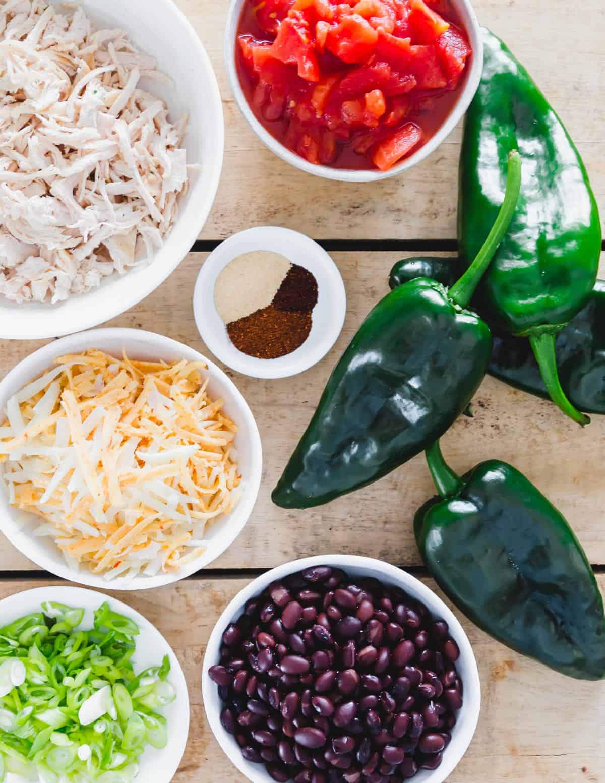 Ingredients to make stuffed poblano peppers including shredded cooked chicken, cheese, black beans, tomatoes and spices.