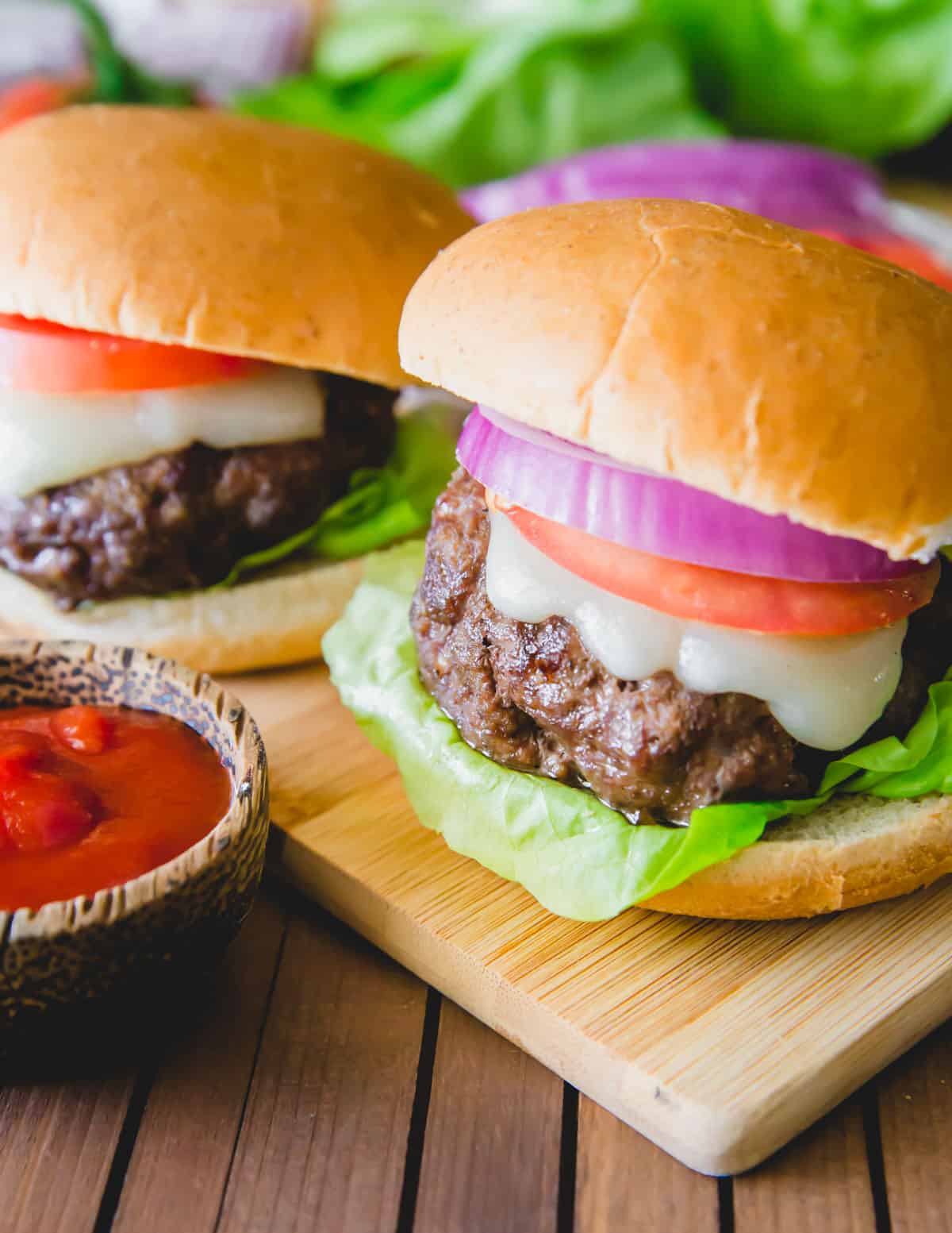 Elk burger made with ground elk meat, ghee and spices on a bun with melted cheese, lettuce, tomato and onion.