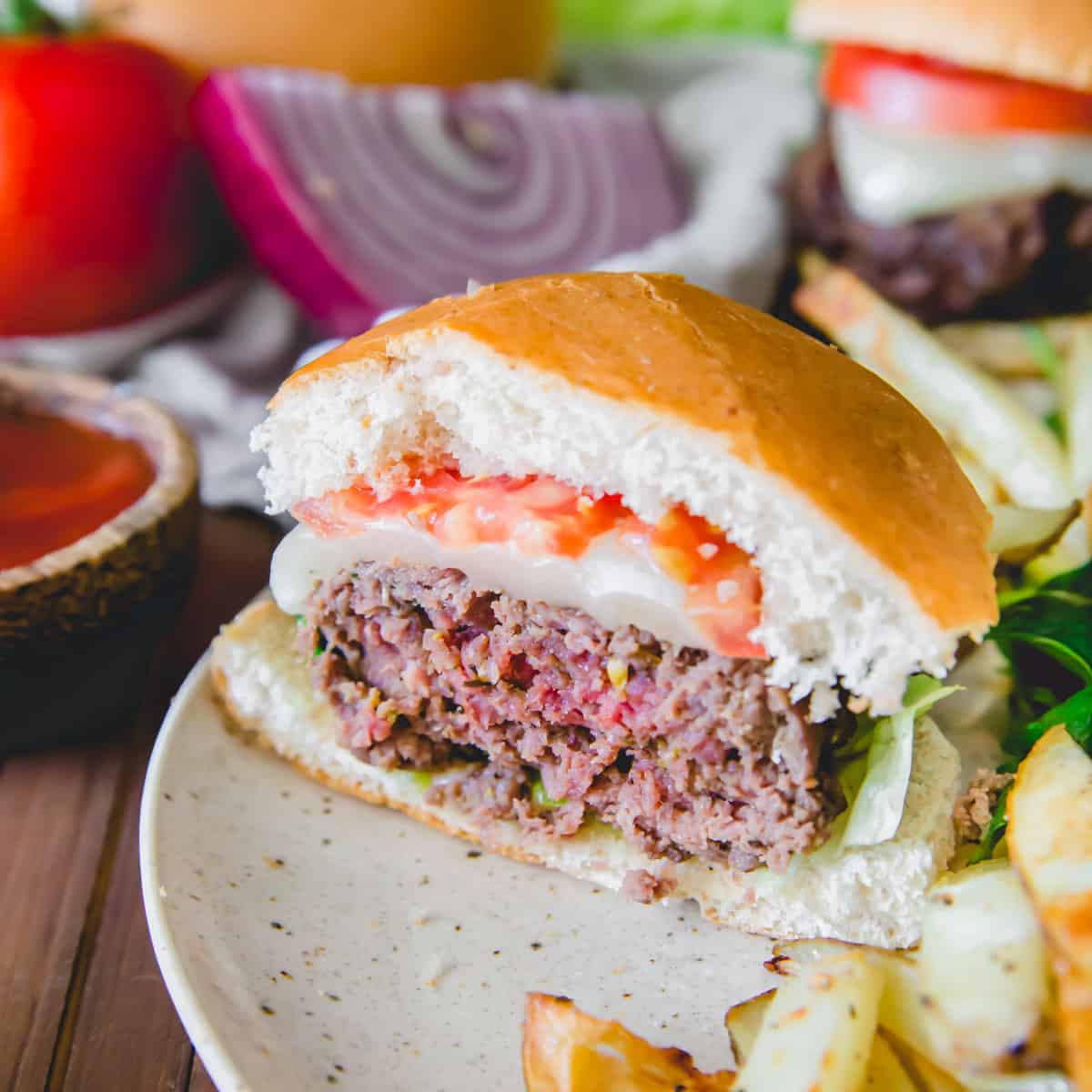 Medium rare elk burger cut in half on a plate with melted cheddar, tomato, lettuce, onion and ketchup.