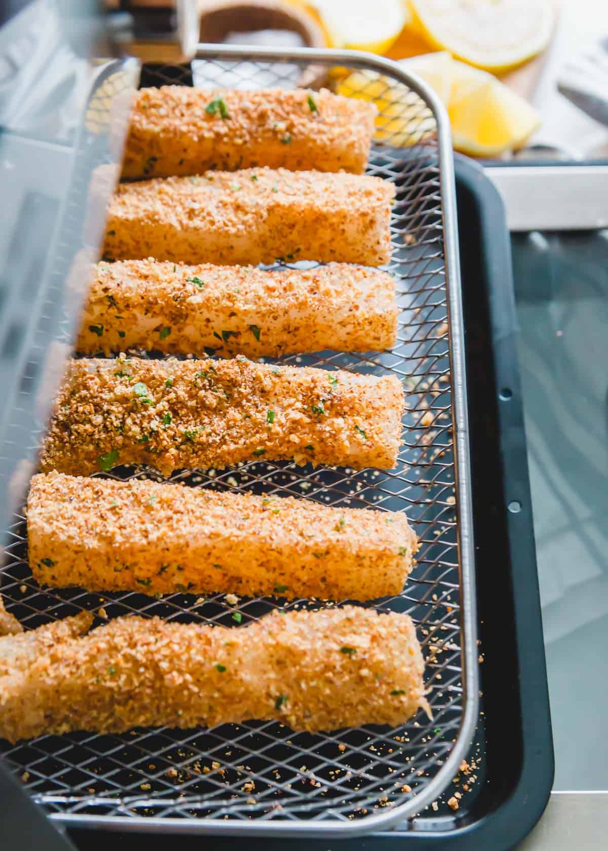 Breadcrumb coated cod is placed on the tray or basket of an air fryer to cook until crispy.