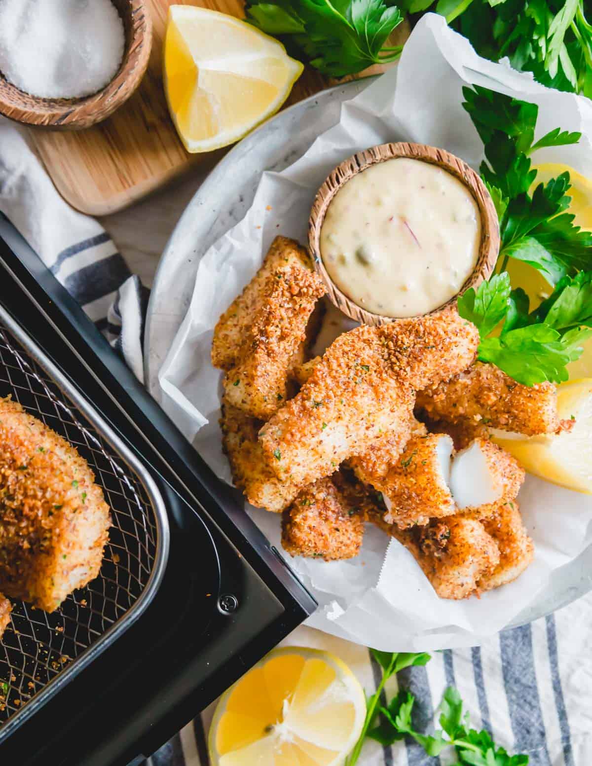 Easy air fryer fish sticks are served with lemon wedges, fresh parsley and an easy dijon remoulade sauce for dipping.
