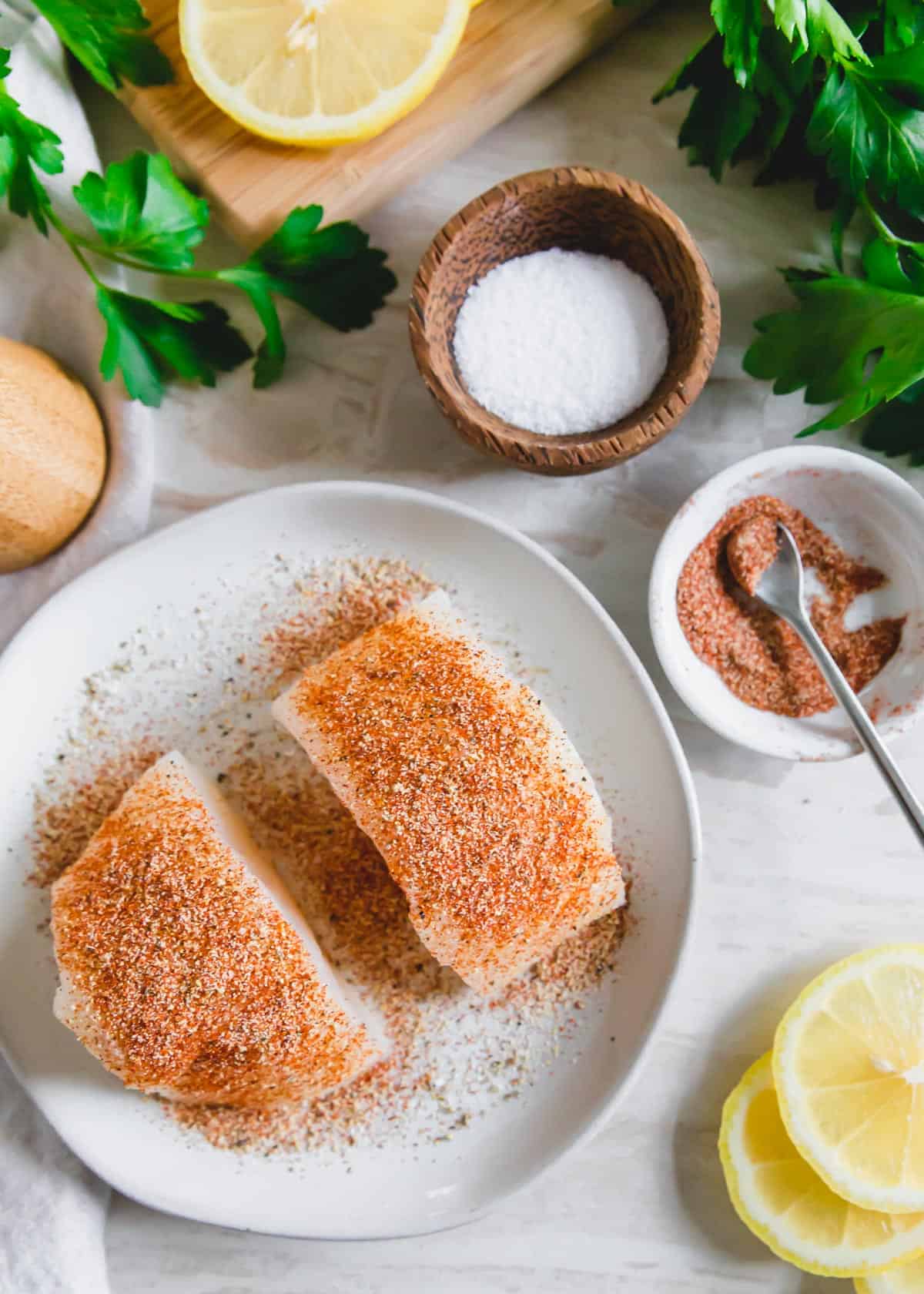 Prepped cod filets seasoned with garlic powder, paprika, cayenne, salt and pepper before air frying.