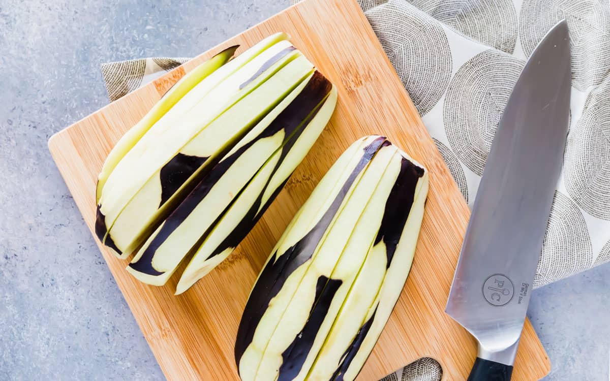 Large peeled eggplant, peeled and sliced on a cutting board.