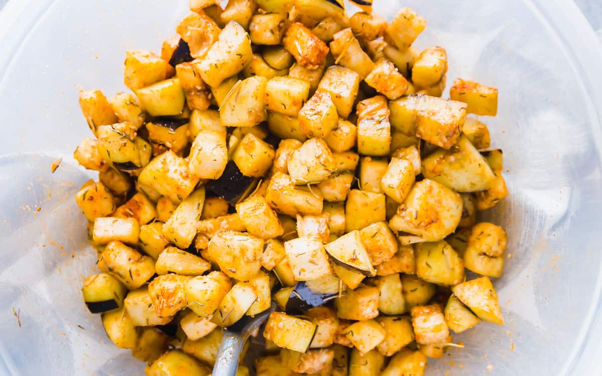 Seasoned eggplant cubes in a large bowl before air frying.