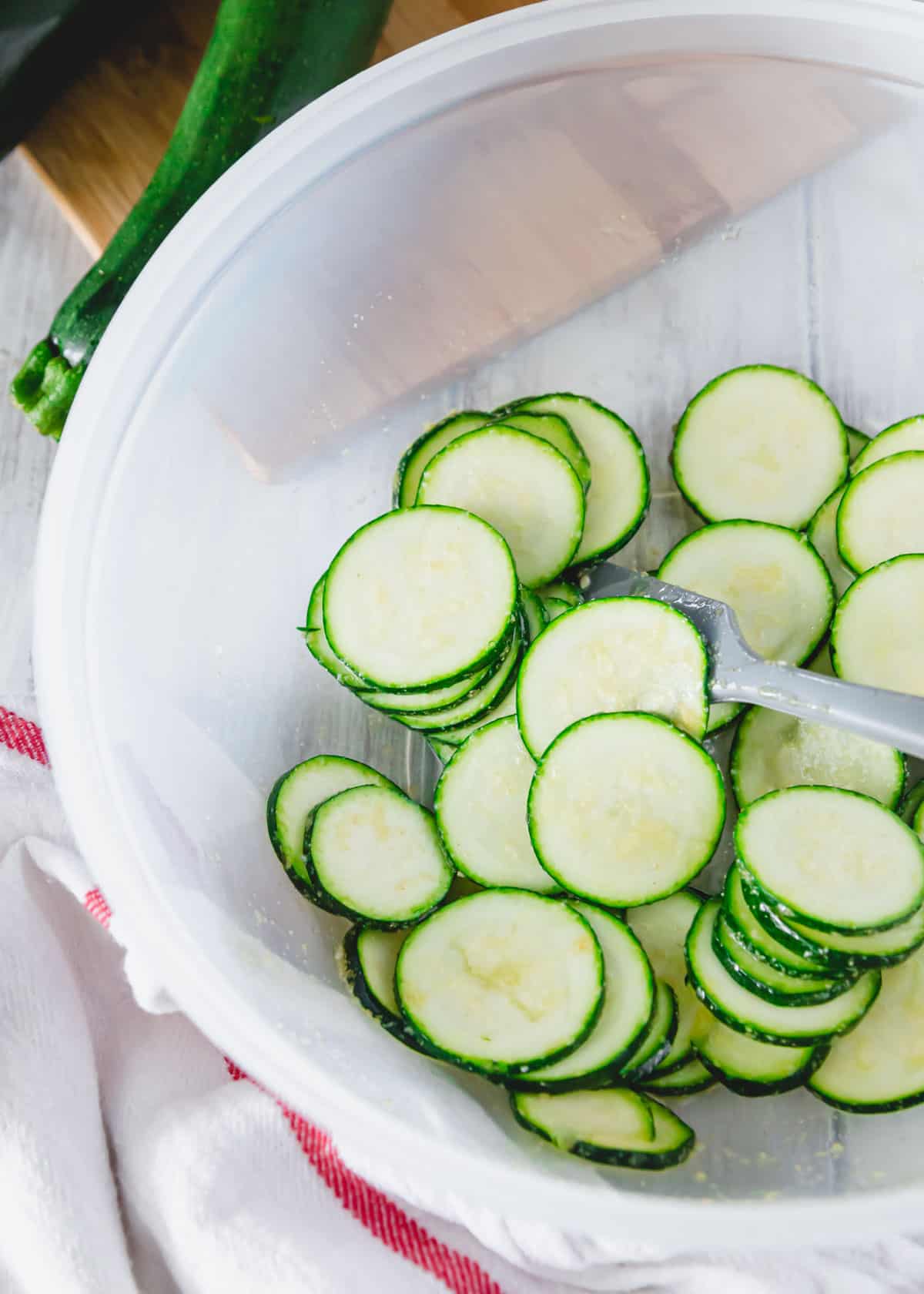 Salted zucchini slices tossed with olive oil and garlic powder in a mixing bowl.