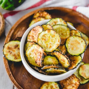 Air fryer zucchini chips in a white bowl on a wooden plate.