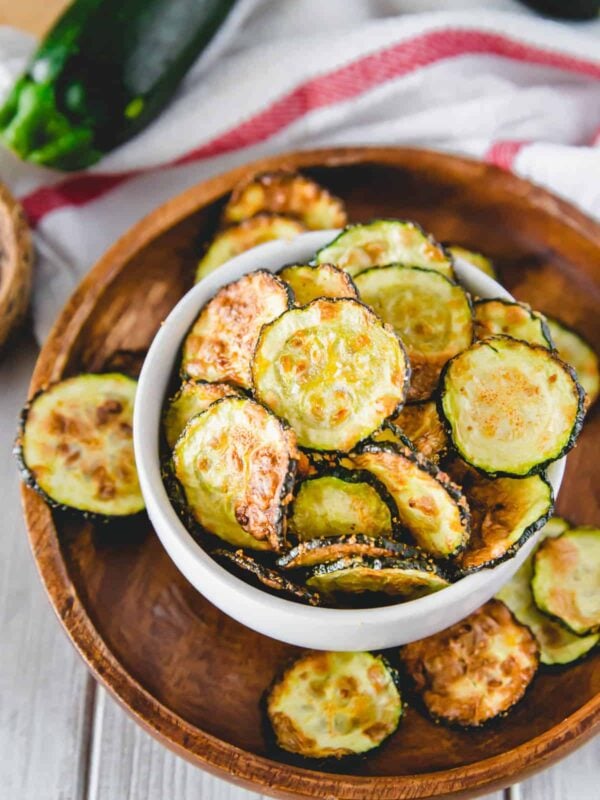 Air fryer zucchini chips in a white bowl on a wooden plate.