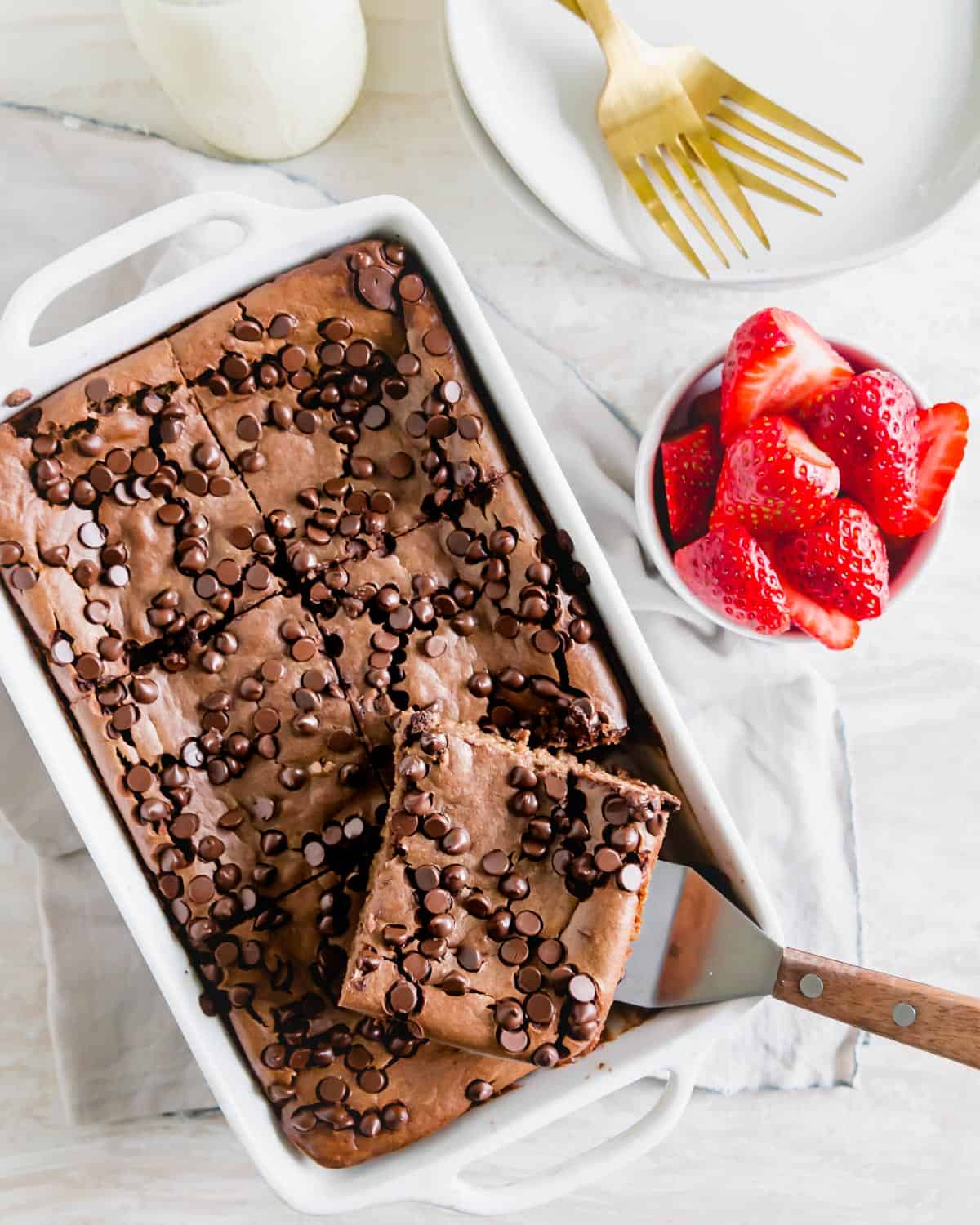 Chocolate baked oats in a baking dish with one slice on a spatula served with fresh strawberries.