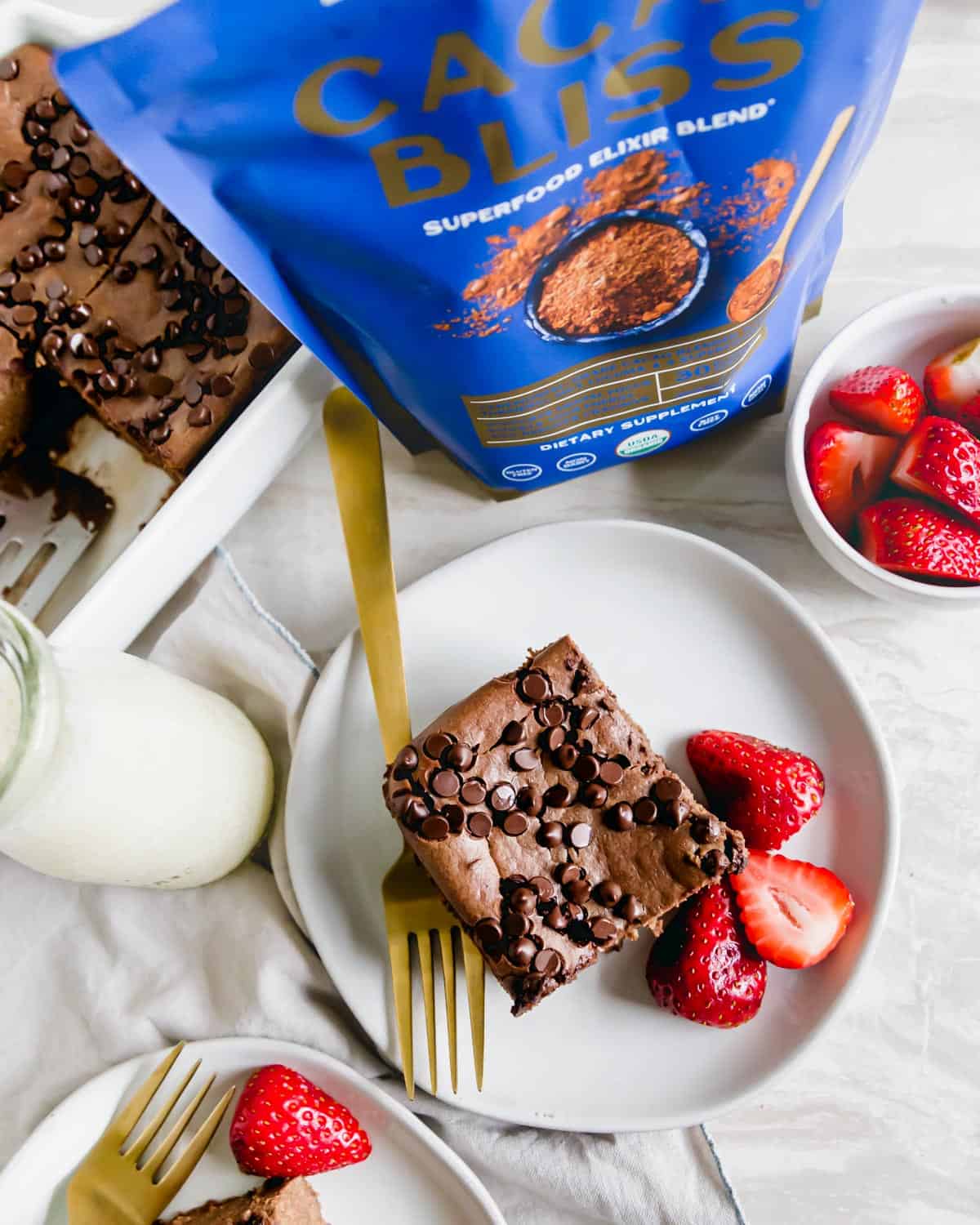 TikTok chocolate baked oats on a serving plate with a bottle of milk and fresh strawberries on the side. Pictured with Cacao Bliss cacao powder in the background.