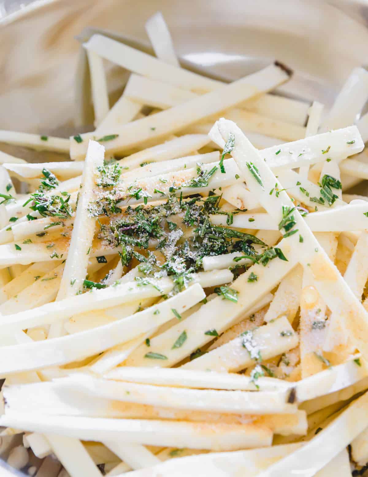 Parsnip "fries" seasoned with freshly chopped rosemary, garlic powder, salt, pepper and avocado oil in a bowl.