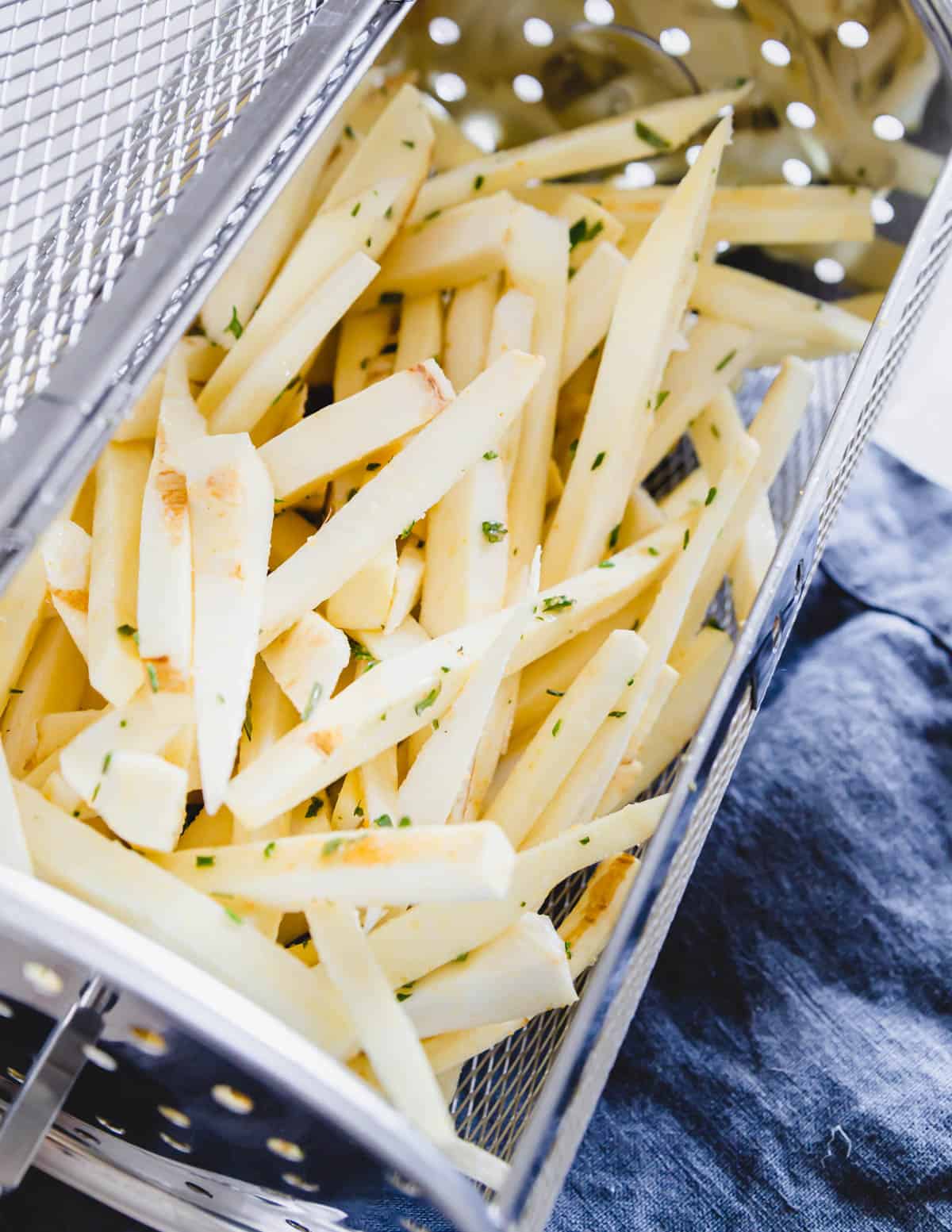 Seasoned raw parsnip fries in an air fryer basket before air frying.