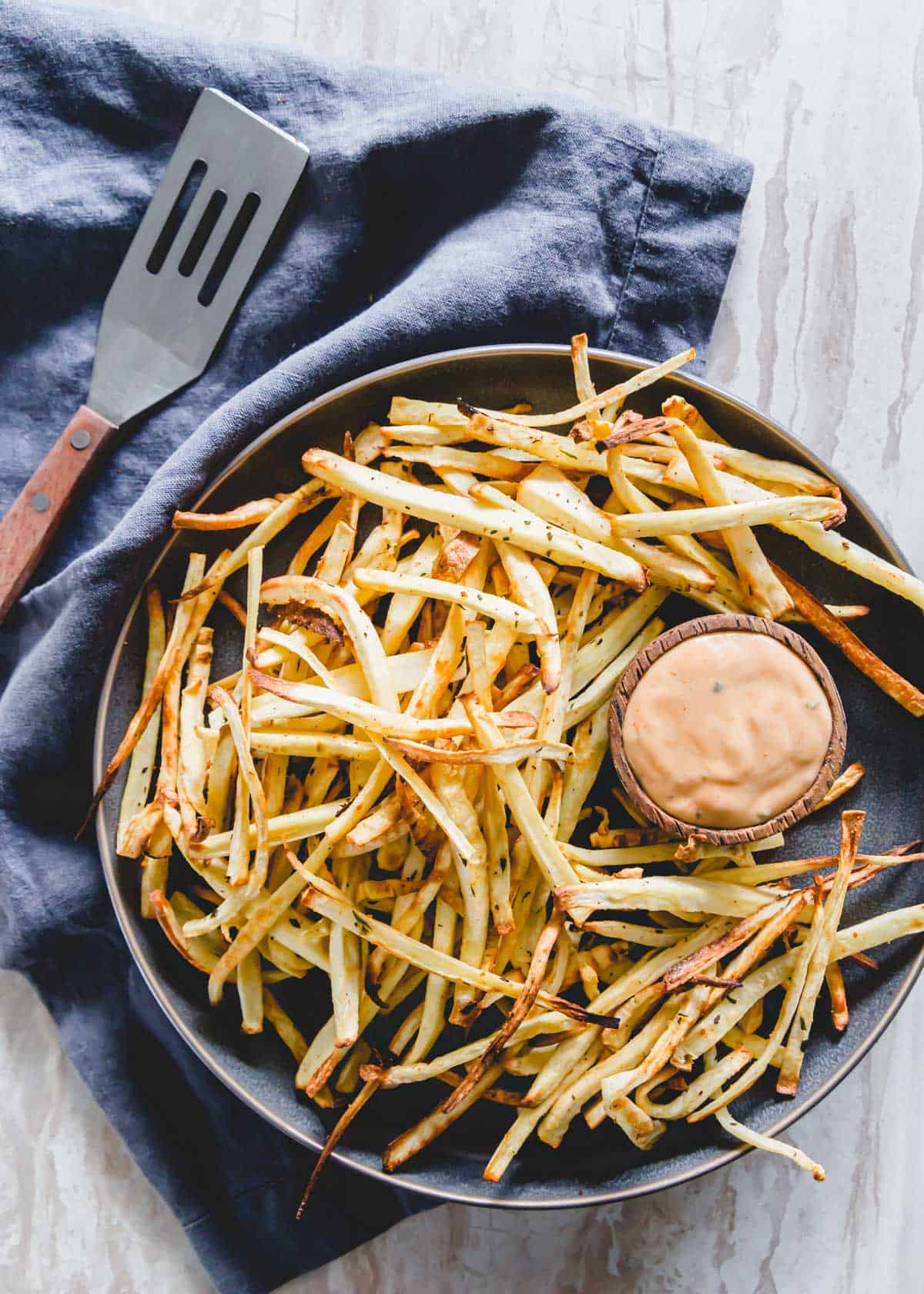 Rosemary garlic baked parsnip fries with a ketchup and mayonnaise dipping sauce on a serving plate.