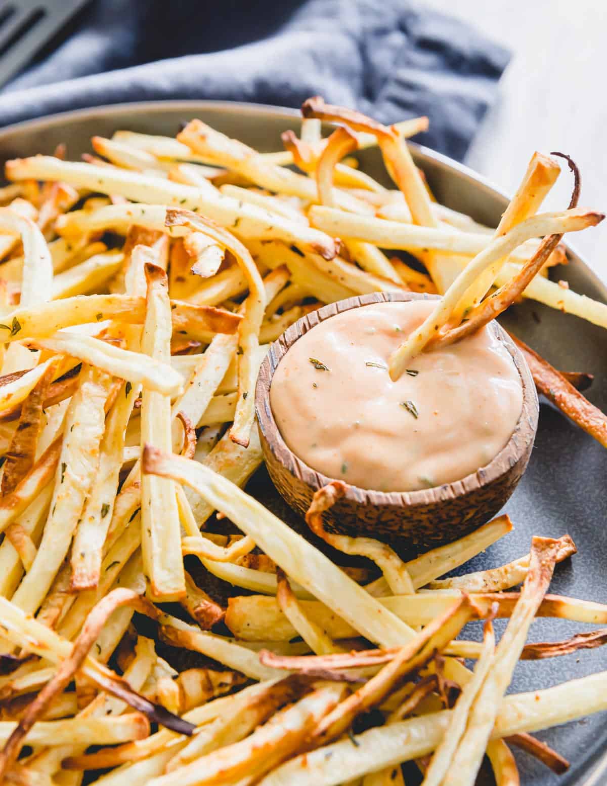 Crispy parsnip fries dipped in a fry sauce on a plate.