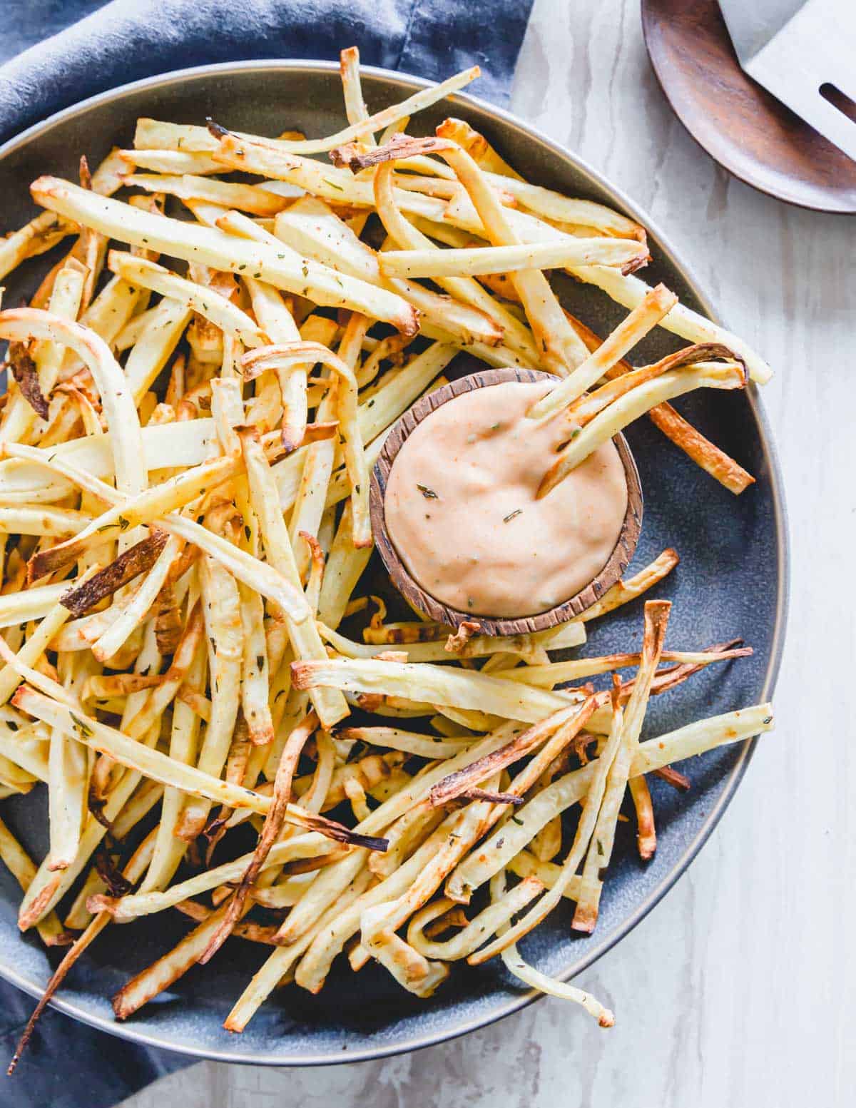 Crispy parsnip fries with rosemary and garlic seasoning served on a plate with an easy fry-sauce.