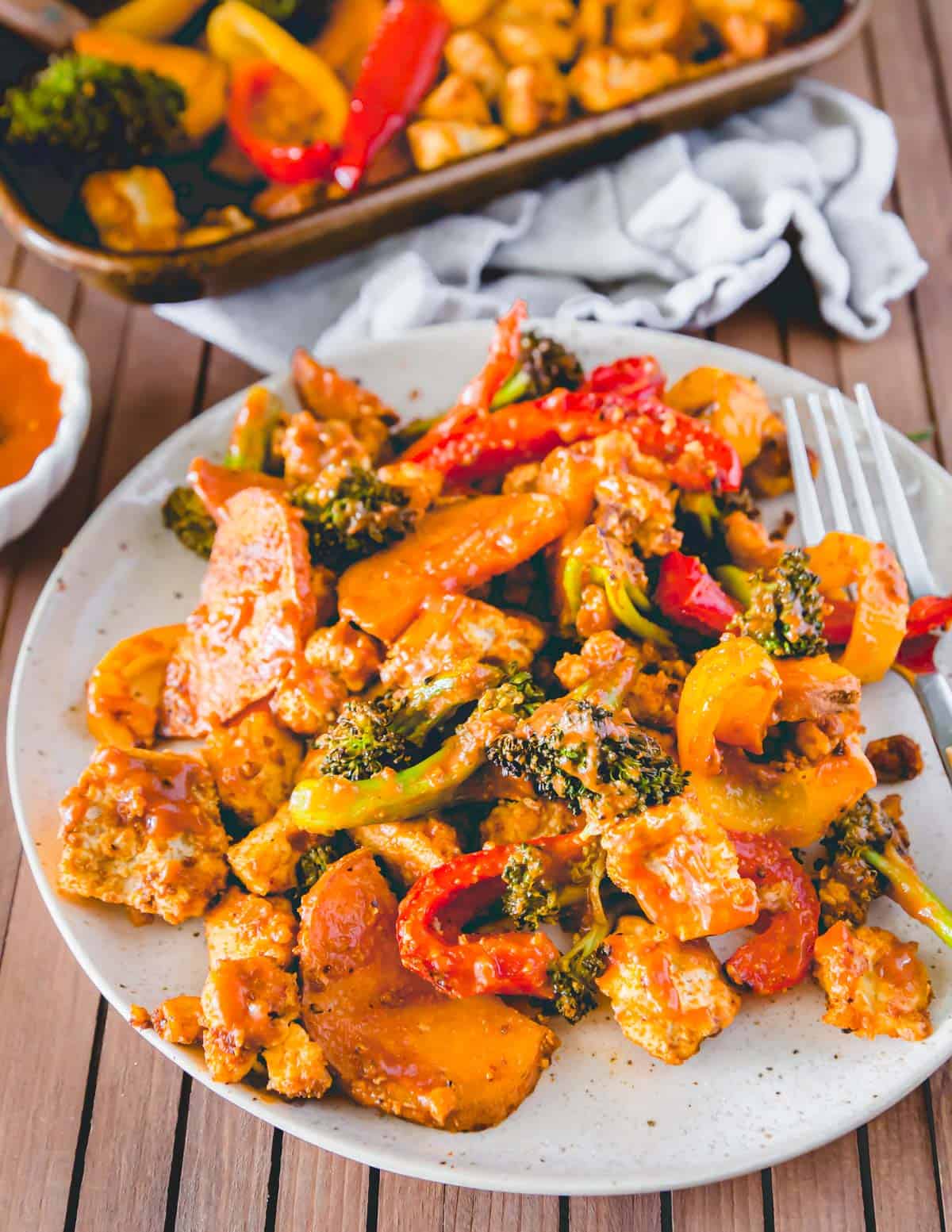 Sheet pan dinner of BBQ tofu, broccoli, peppers and sweet potatoes served on a plate.