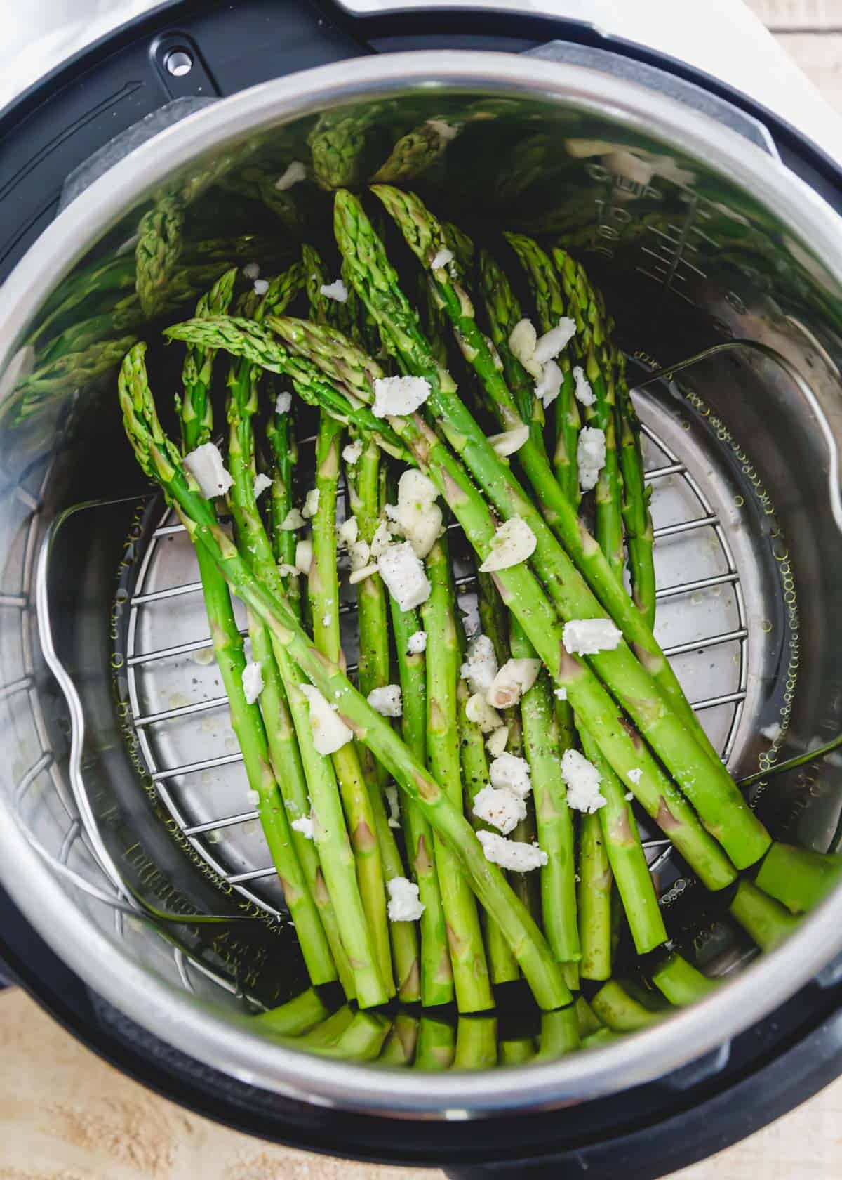 Raw asparagus spears in an Instant Pot with olive oil, butter and garlic on top and water on the bottom of the insert.