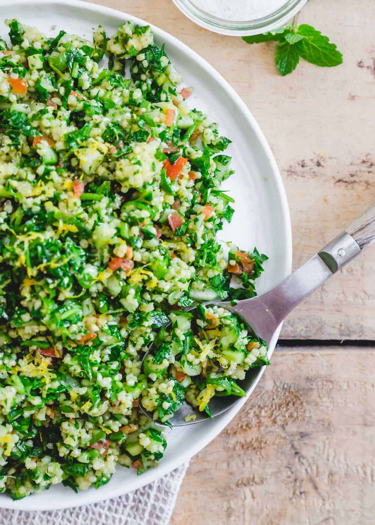 Millet tabbouleh on a white plate with a wooden serving spoon.