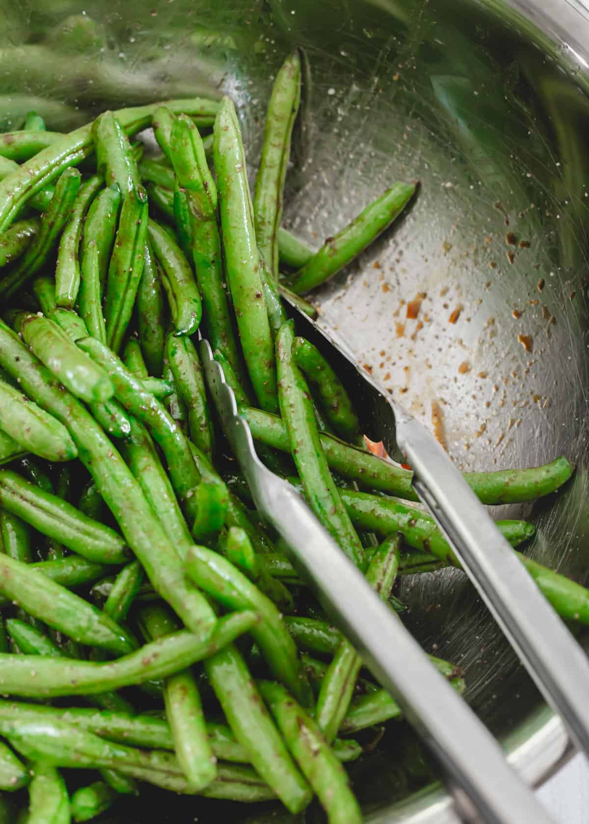 Green beans with avocado oil, tamari, garlic powder, salt and pepper in a metal bowl.