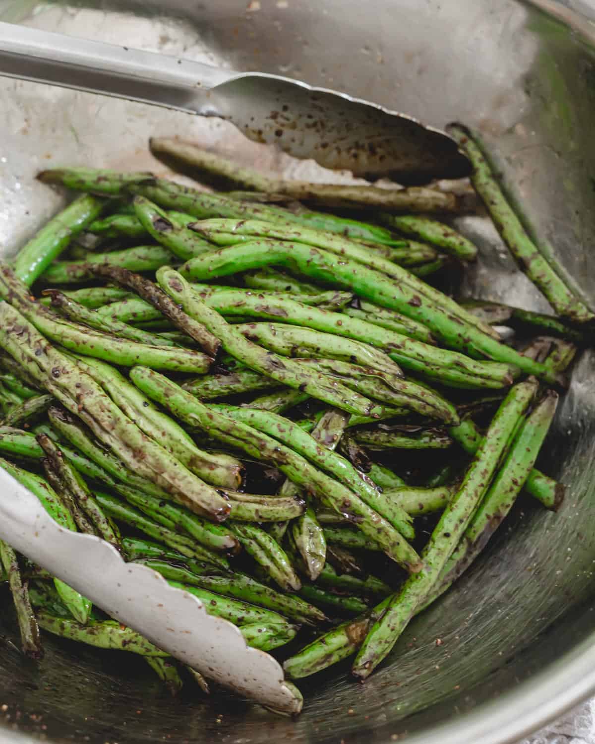 Garlic soy grilled green beans in a bowl with metal tongs.