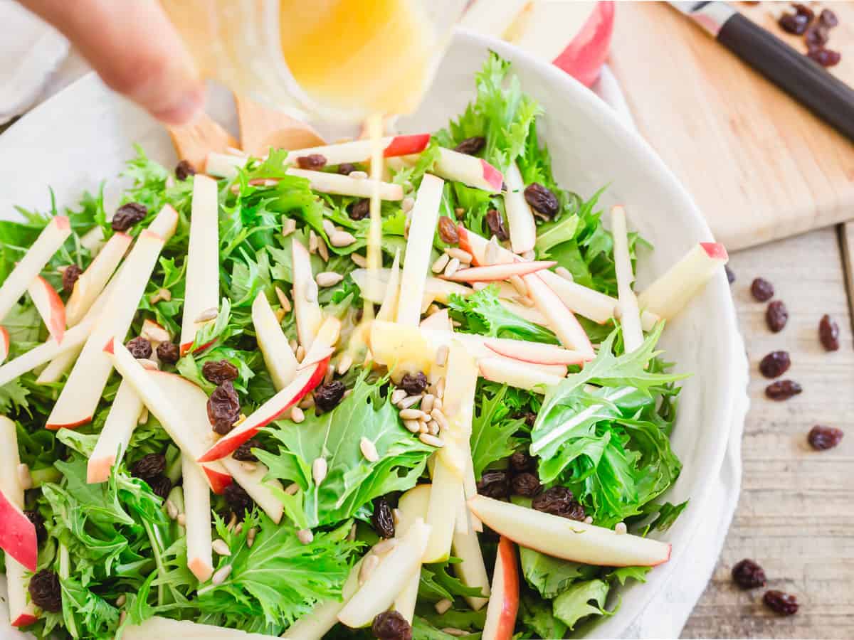 Lemon honey dijon dressing being poured over mizuna salad in a bowl.