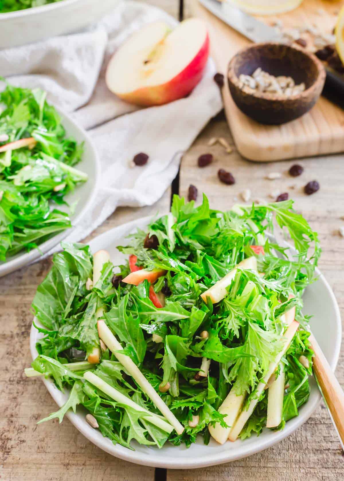 Crisp mizuna lettuce salad dressed in a lemon honey dijon vinaigrette with apples, raisins and sunflower seeds on a plate with a fork.