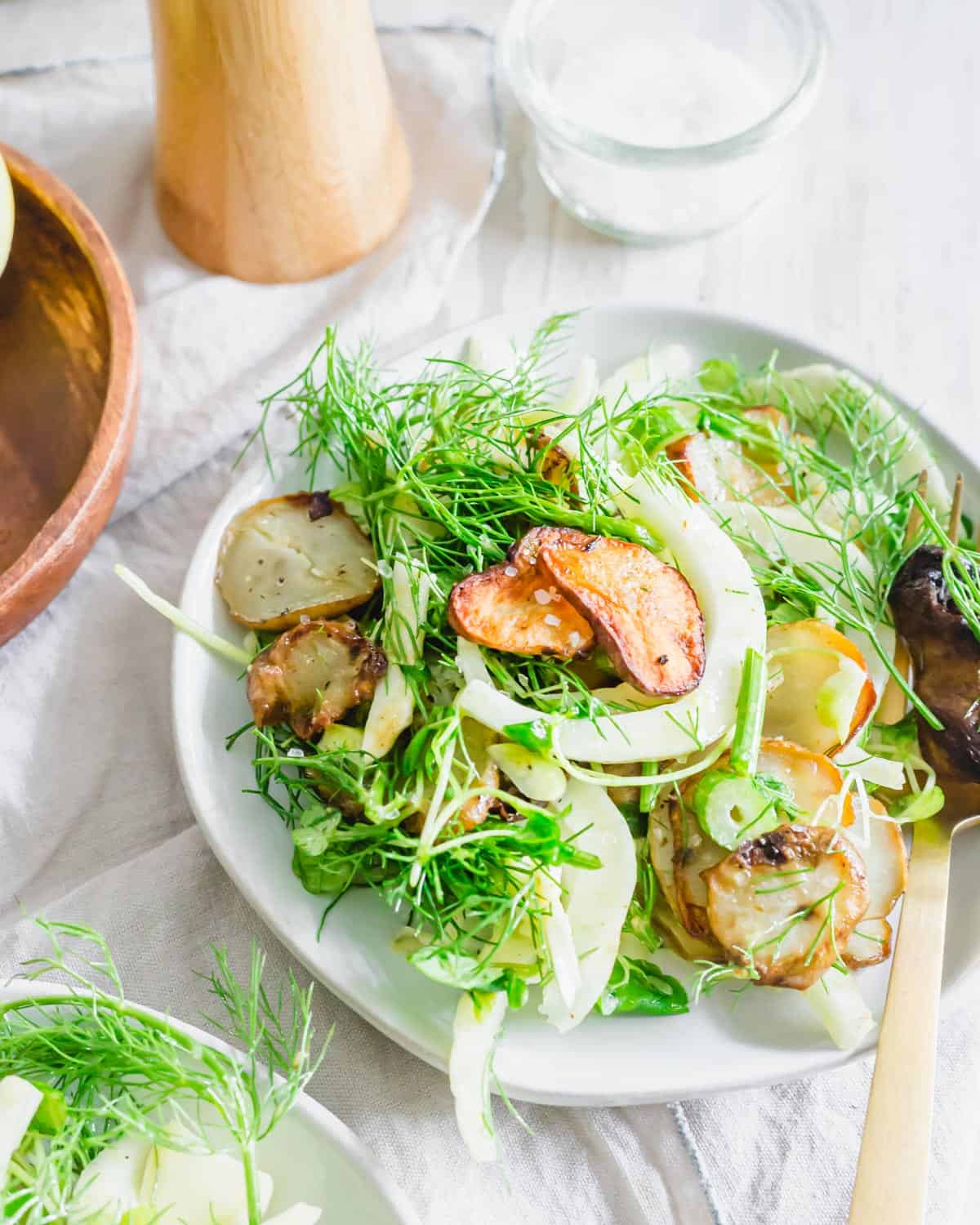 Fennel and arugula salad with roasted sunchokes tossed in a lemon mustard dressing on a plate garnished with flaky sea salt.