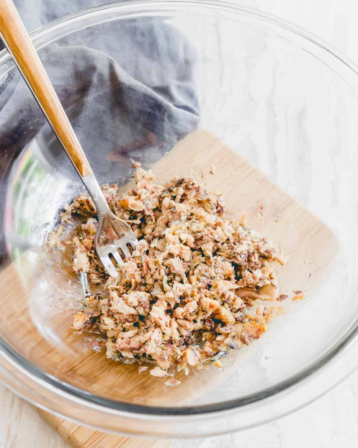 Tinned wild sardines mashed in a glass bowl with a fork.