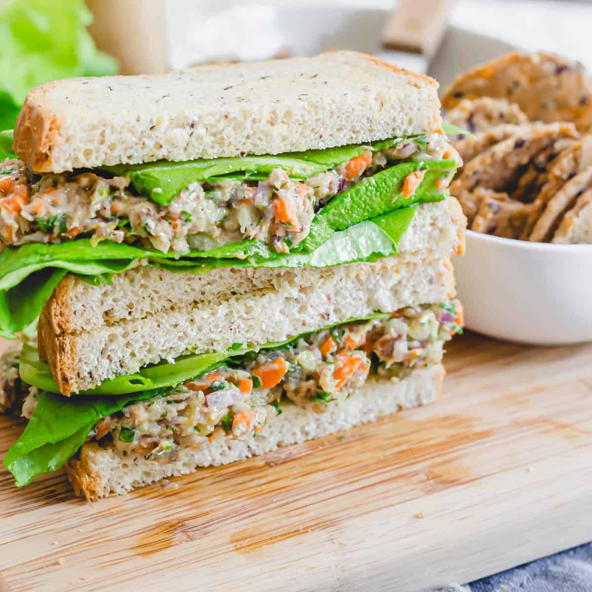 Sardine salad sandwich cut in half and stacked on top of each other on a cutting board.