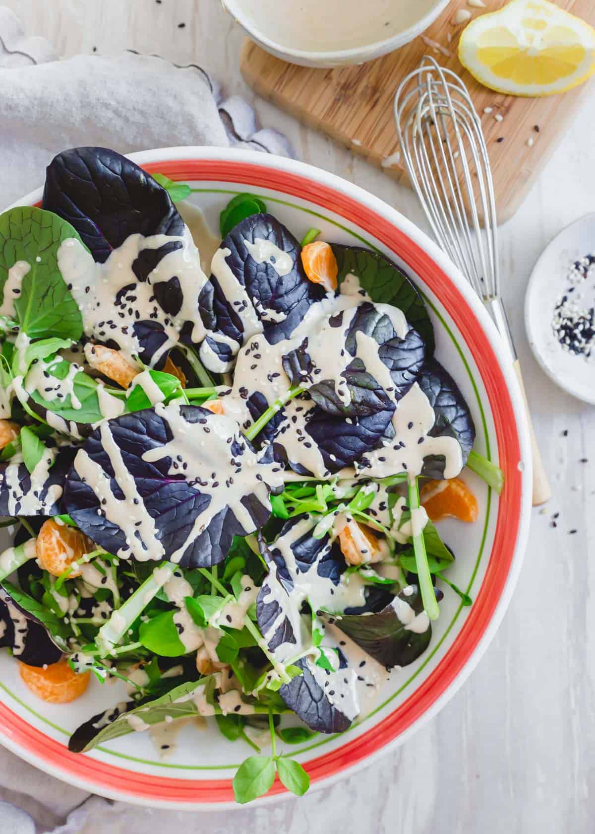 Purple tatsoi salad recipe in a bowl with pea shoots and clementines in a creamy tahini dressing.