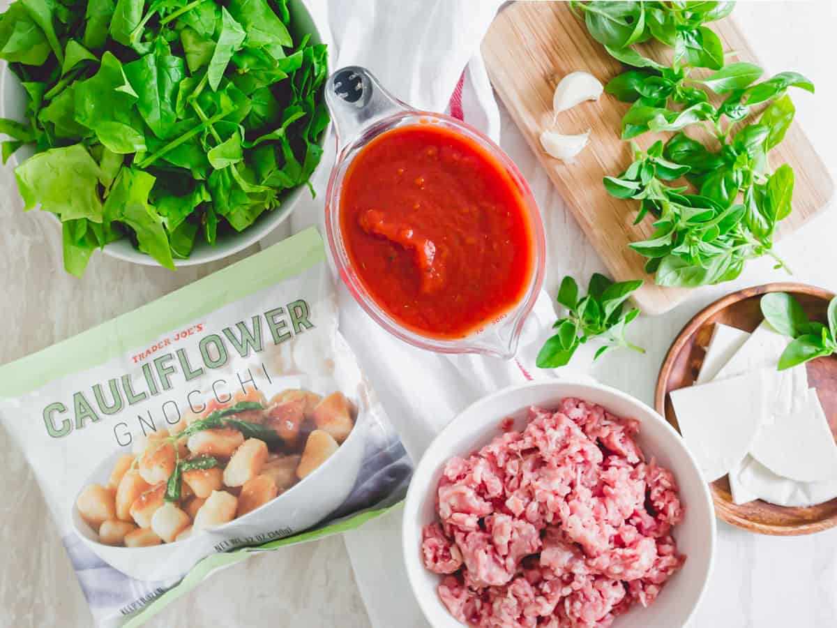 Cauliflower gnocchi recipe ingredients: fresh spinach, crushed tomatoes, ground pork, garlic, Trader Joe's cauliflower gnocchi, sliced mozzarella and fresh basil.