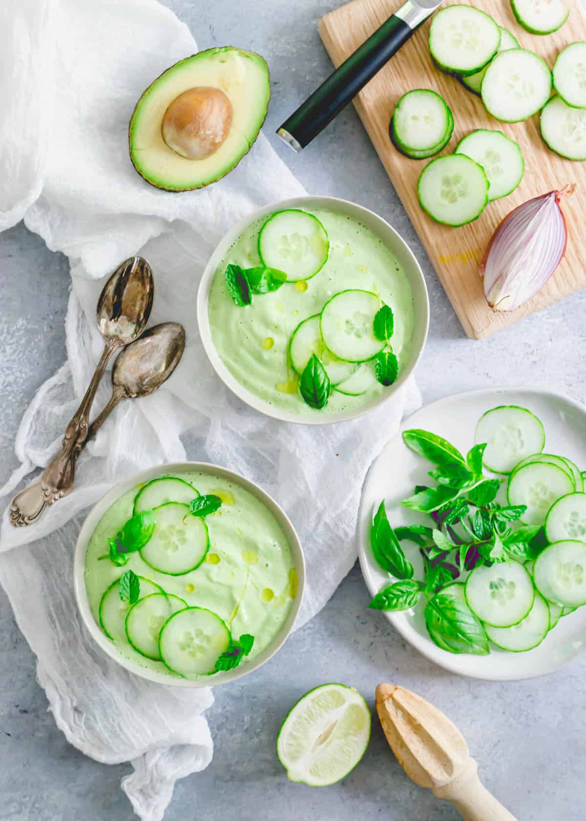 Chilled cucumber gazpacho in bowls with fresh cucumber slices, mint and basil.