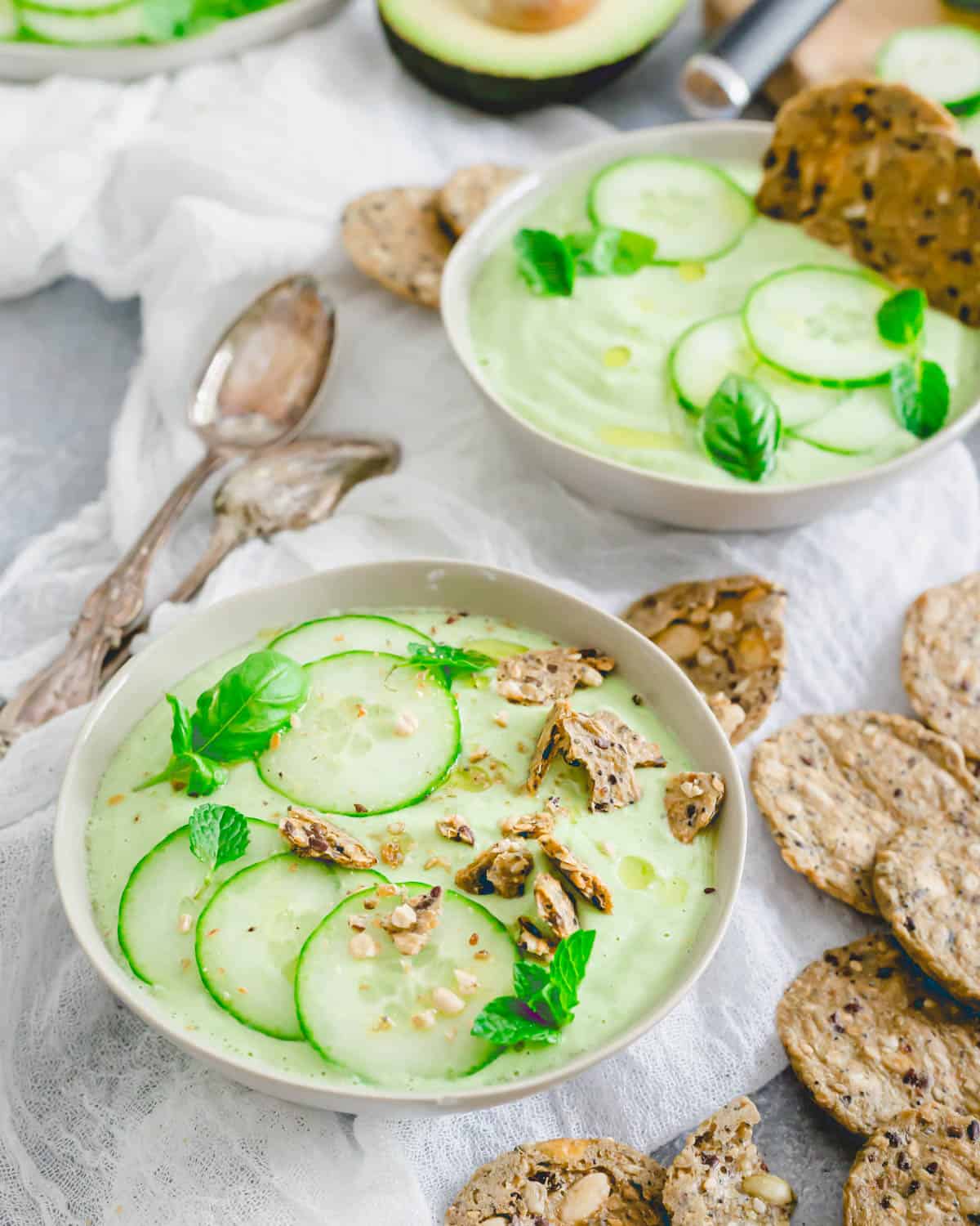 Creamy cucumber gazpacho recipe in bowls with crunchy gluten-free crackers on top.