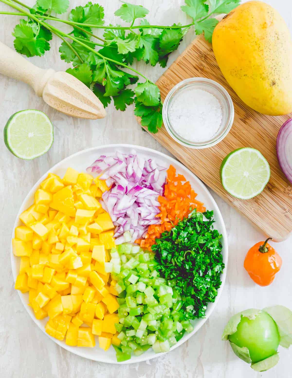 Finely chopped mango, red onion, habanero pepper, cilantro and tomatillo on a plate prepped for mango habanero salsa.