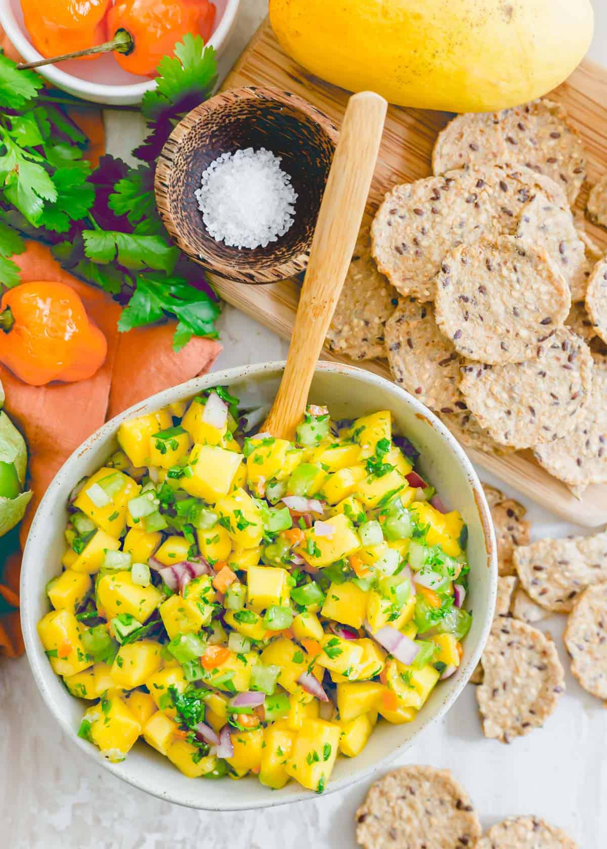 Fresh mango salsa with habanero peppers in a bowl with crackers on the side for serving.