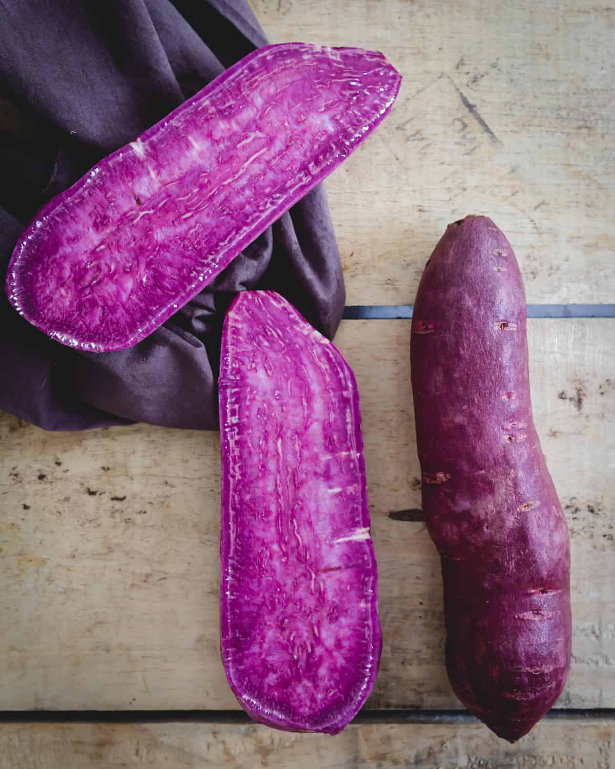 Stokes purple sweet potatoes, one whole, one cut in half on a wooden board.