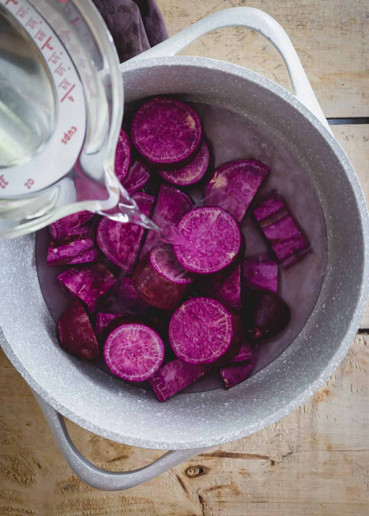 Sliced Japanese purple sweet potatoes in a pot with cold water before boiling.