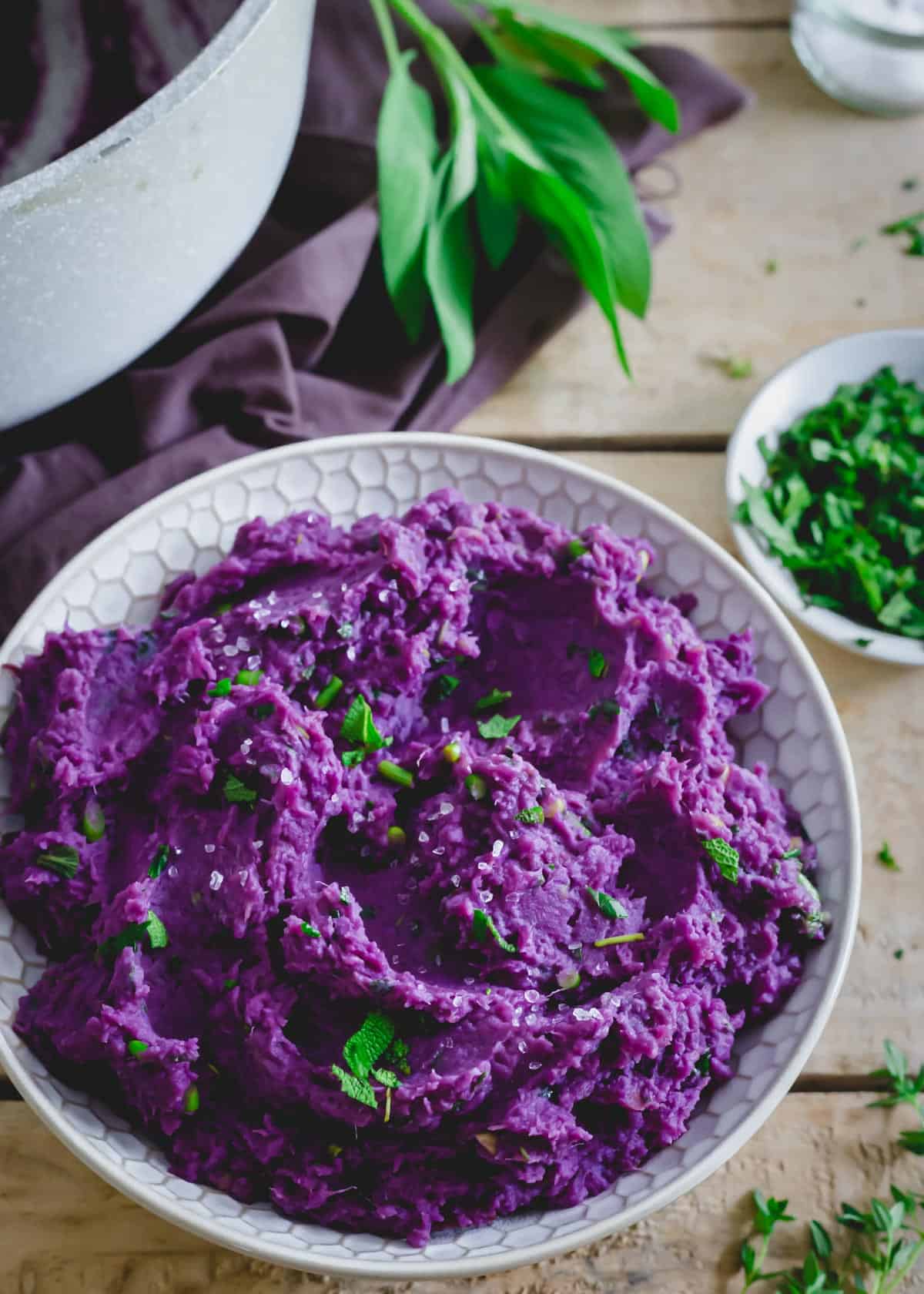 Creamy purple mashed sweet potatoes in a dish with herb butter sauce and sea salt.