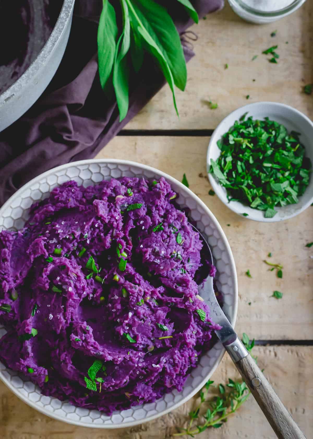 Easy mashed purple potatoes with herb butter sauce in a bowl with a serving spoon.