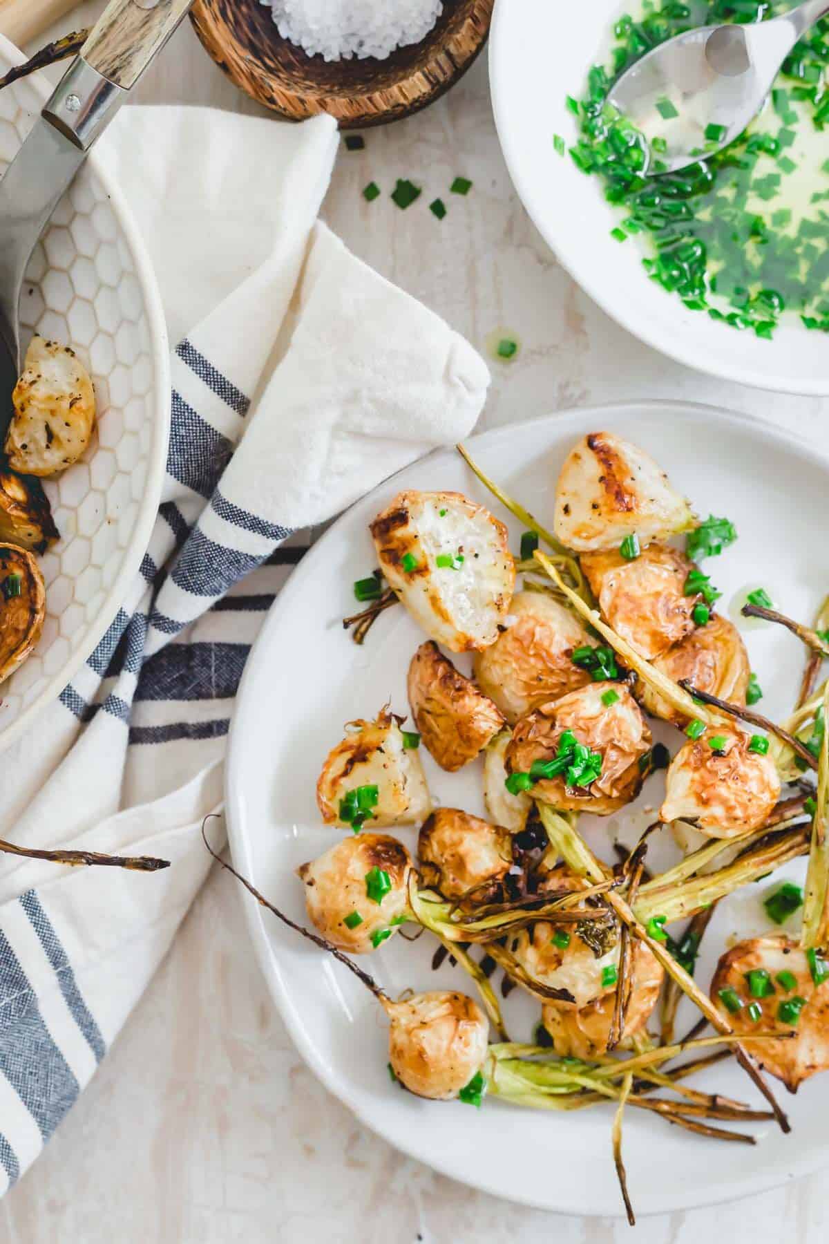 Oven roasted white turnips and stems on a plate with a ghee and chive sauce.