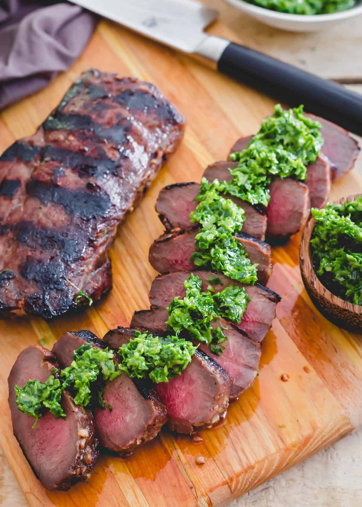 Easy recipe for deer backstrap marinated, grilled and sliced on a cutting board with pesto.