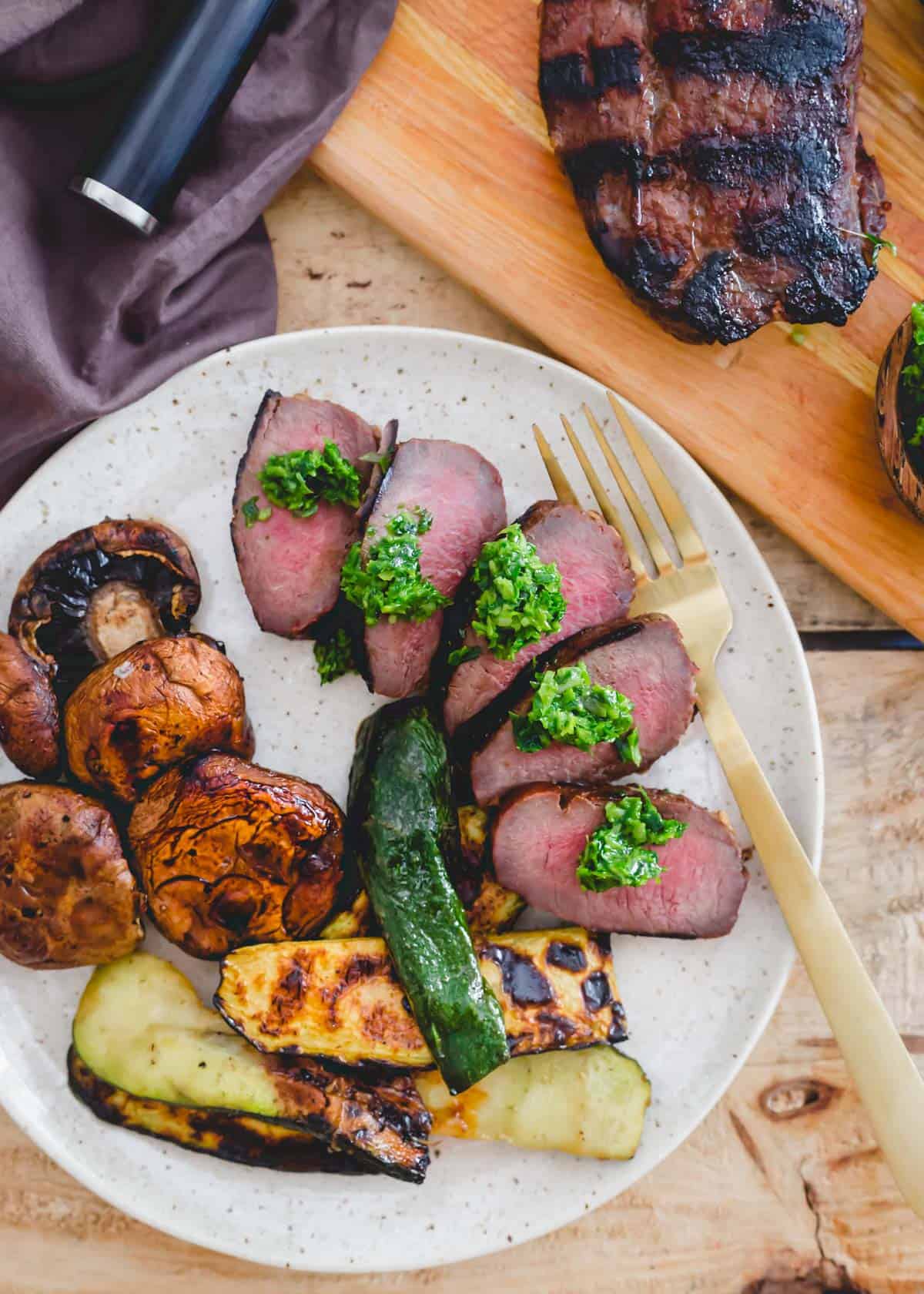 Grilled venison backstrap sliced on a plate with grilled vegetables on the side.