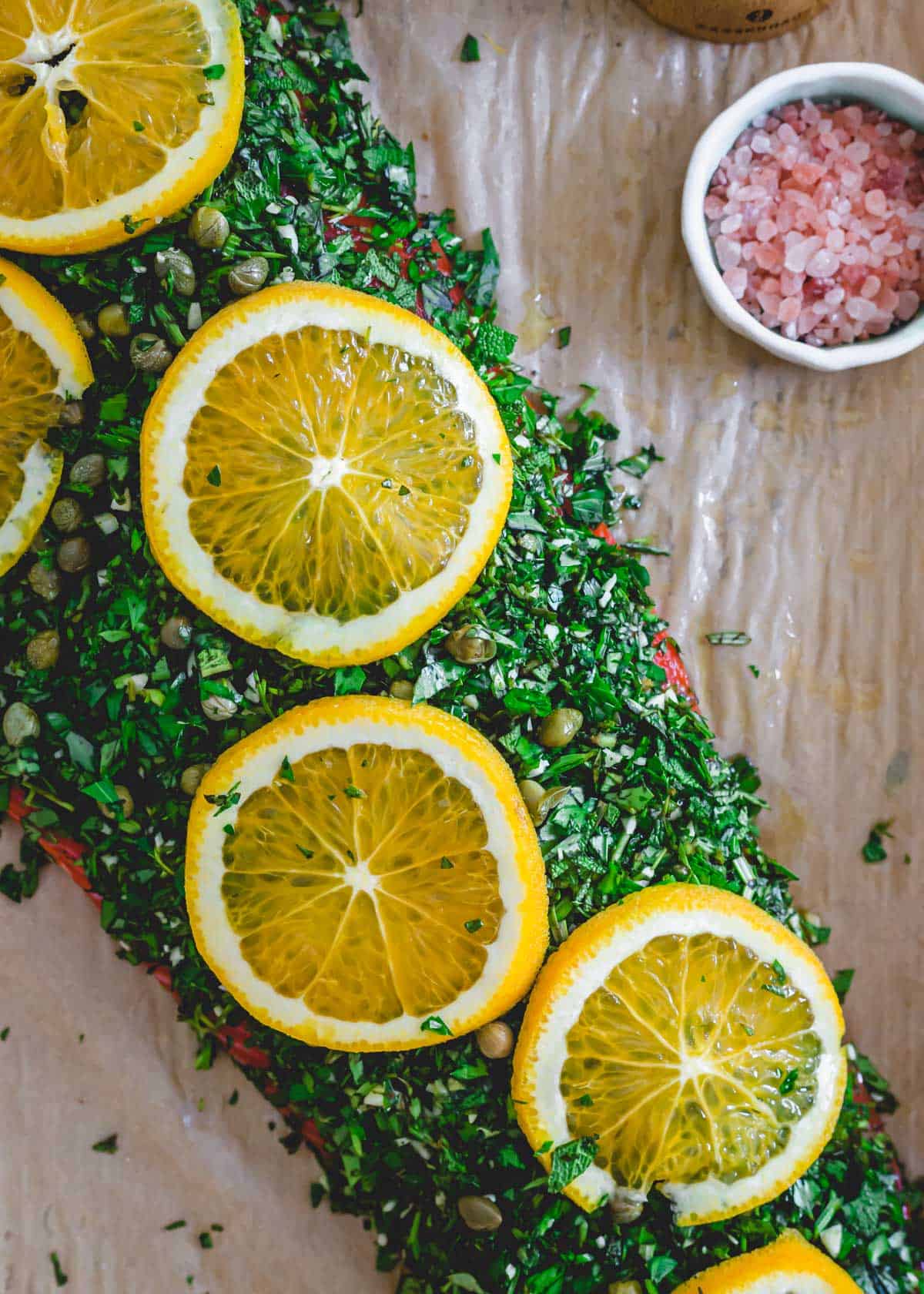 Herb, garlic and caper crusted wild sockeye salmon topped with fresh orange slices on a baking sheet before being cooked.