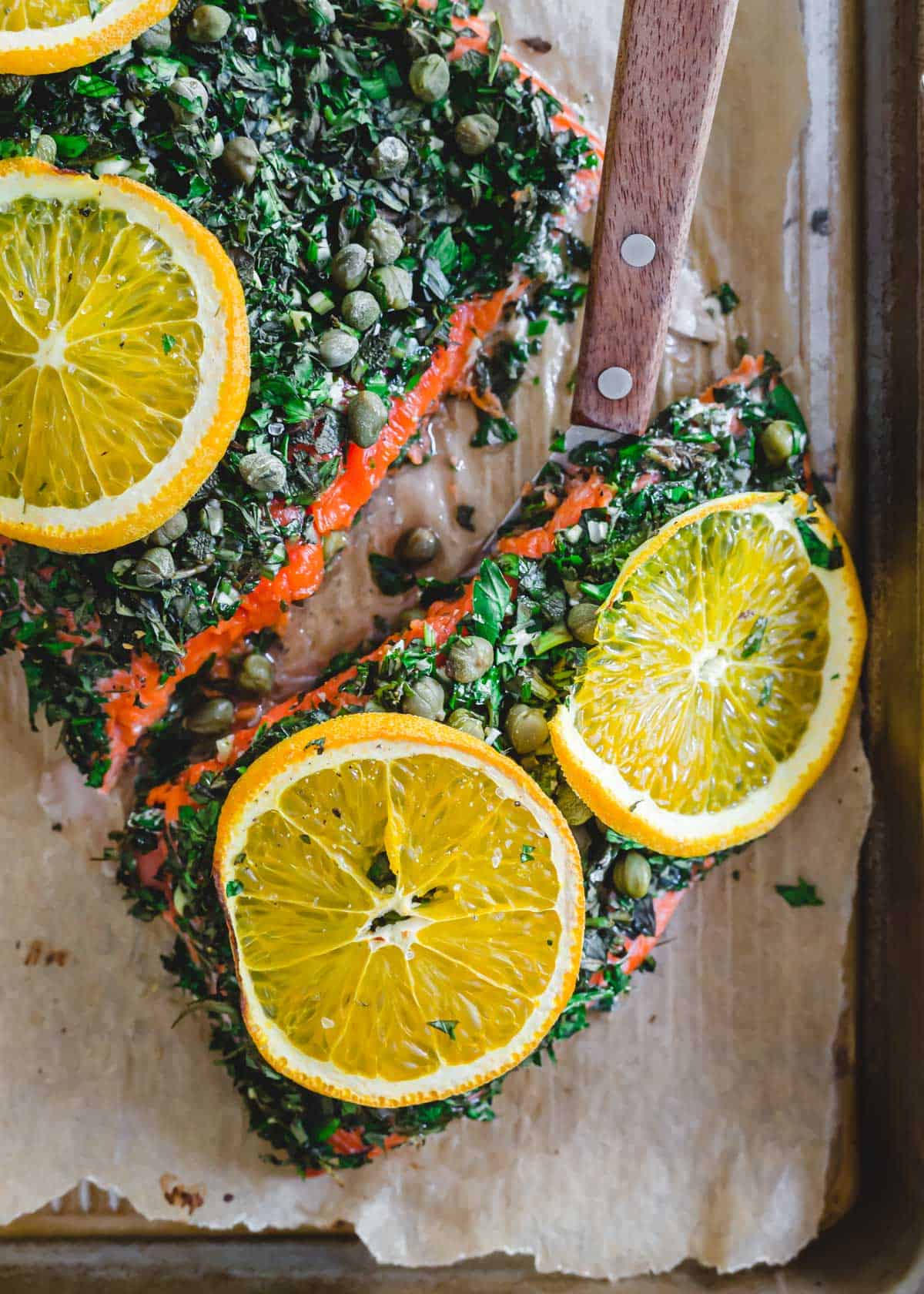 Baked wild sockeye salmon with herbs and fresh orange slices on a baking sheet.