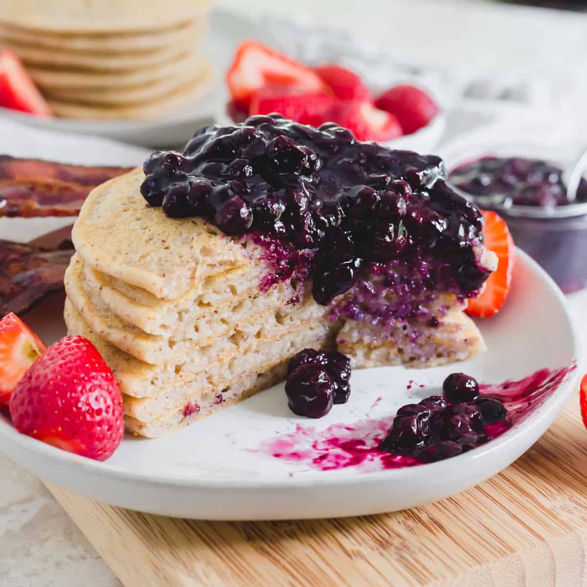 Paleo cassava and tigernut flour pancakes on a plate with blueberry compote, fresh strawberries and bacon.