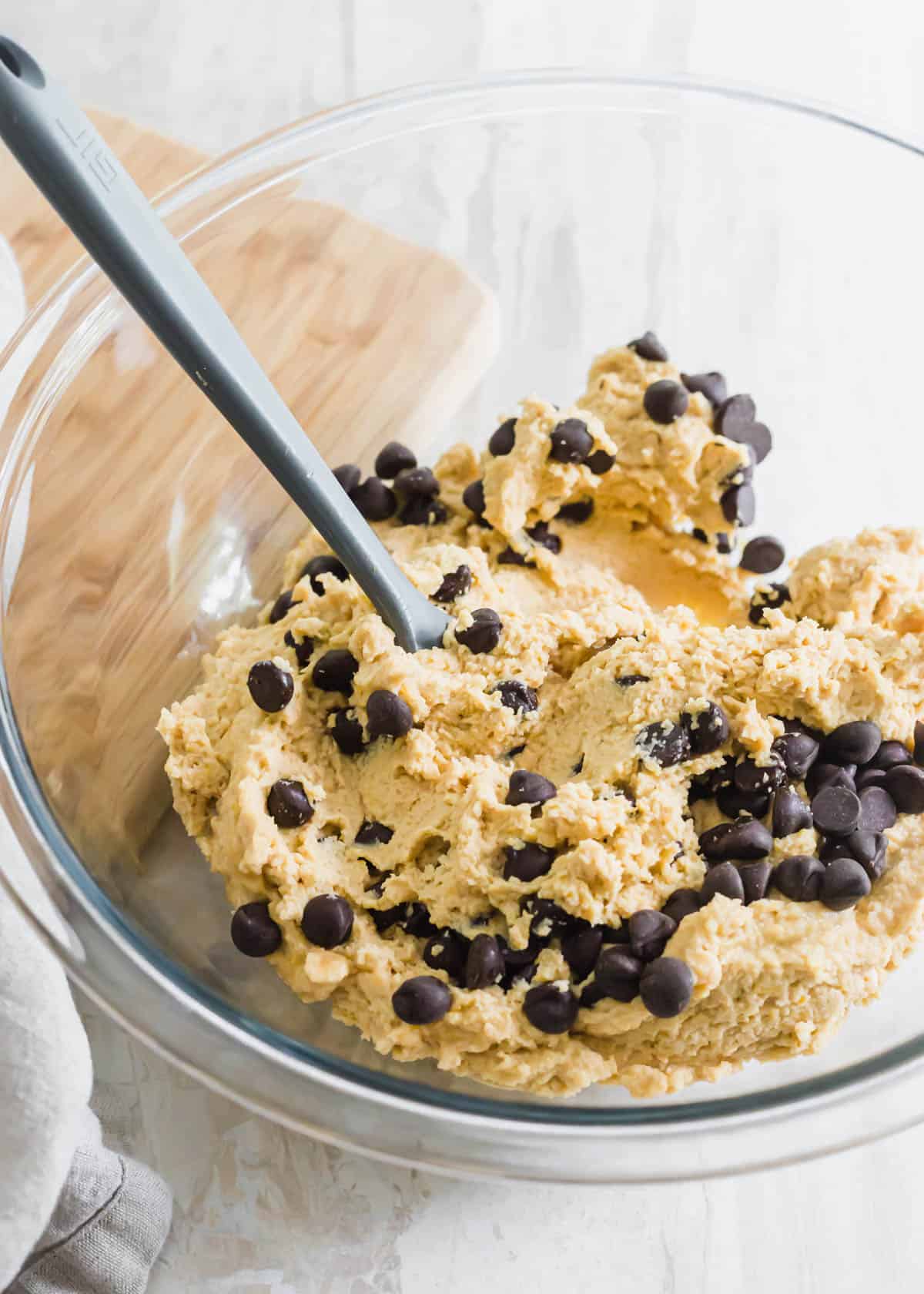 Chickpea blondie cookie dough batter in a glass bowl with chocolate chips mixed in.