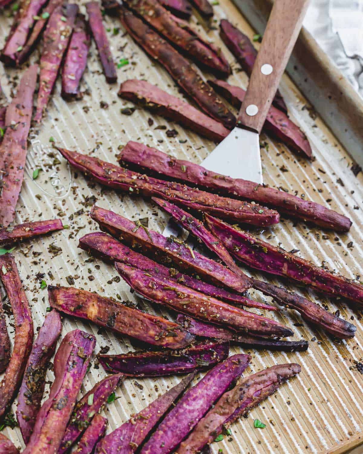 Baked purple sweet potato fries on a baking sheet with spatula.