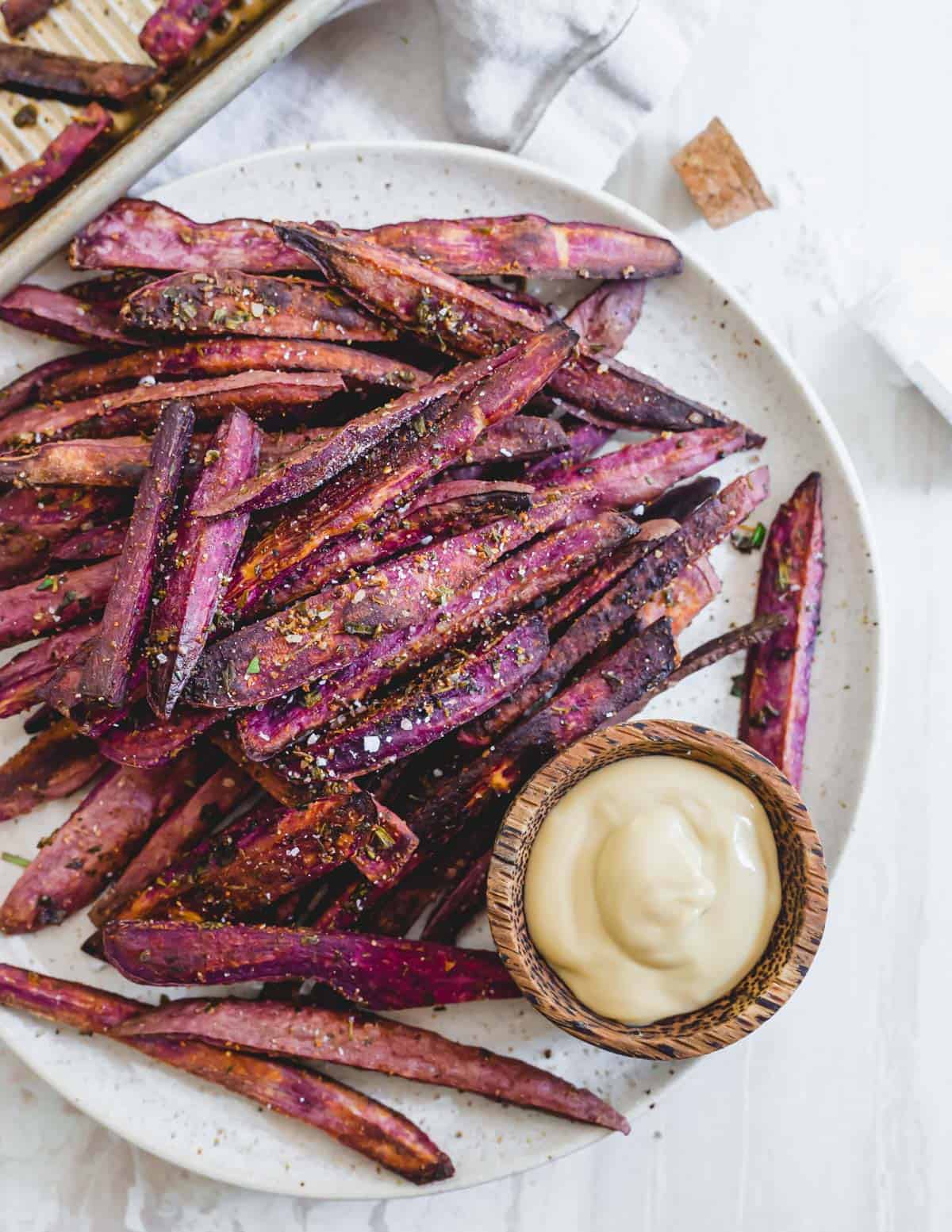 Crispy oven baked purple sweet potato fries with fresh herbs and sea salt on a plate.