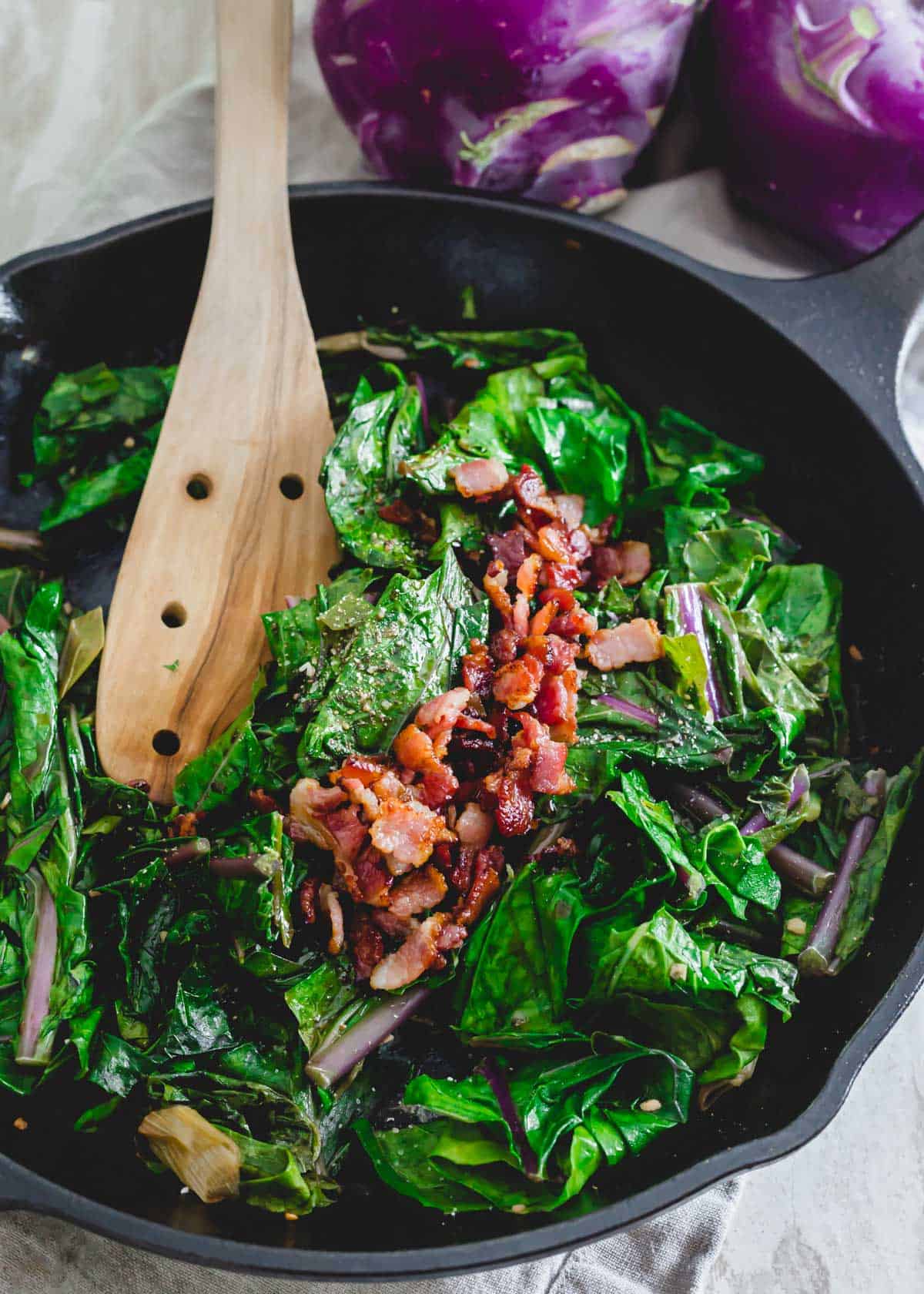 Sautéed kohlrabi greens with bacon in a cast iron skillet.