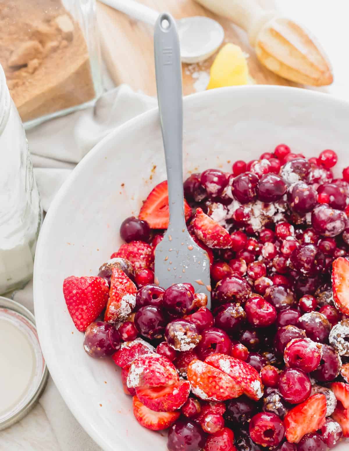 Tart cherries, strawberries and red currants in a bowl with lemon juice, coconut sugar and arrowroot powder to make sour cherry crisp.