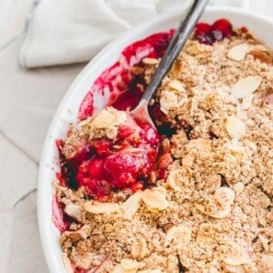Sour cherry crisp in a white baking dish with a spoon.